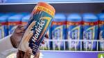 Someone holding a 500g Classic Horlicks and a shelf full of Horlicks in the background